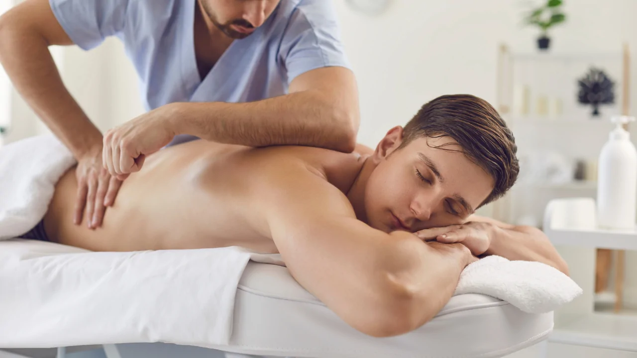 A clinician in a light blue tunic performing a manual therapy technique on a male patient's back to provide chiropractic-led physical therapy at Spine and Joint Center in Fort Lauderdale.