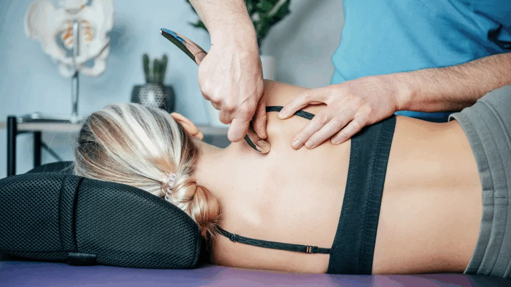 A chiropractor using a stainless steel IASTM tool to perform deep tissue mobilization on a patient's upper back and neck to provide chiropractic massage therapy at Spine and Joint Center in Fort Lauderdale.