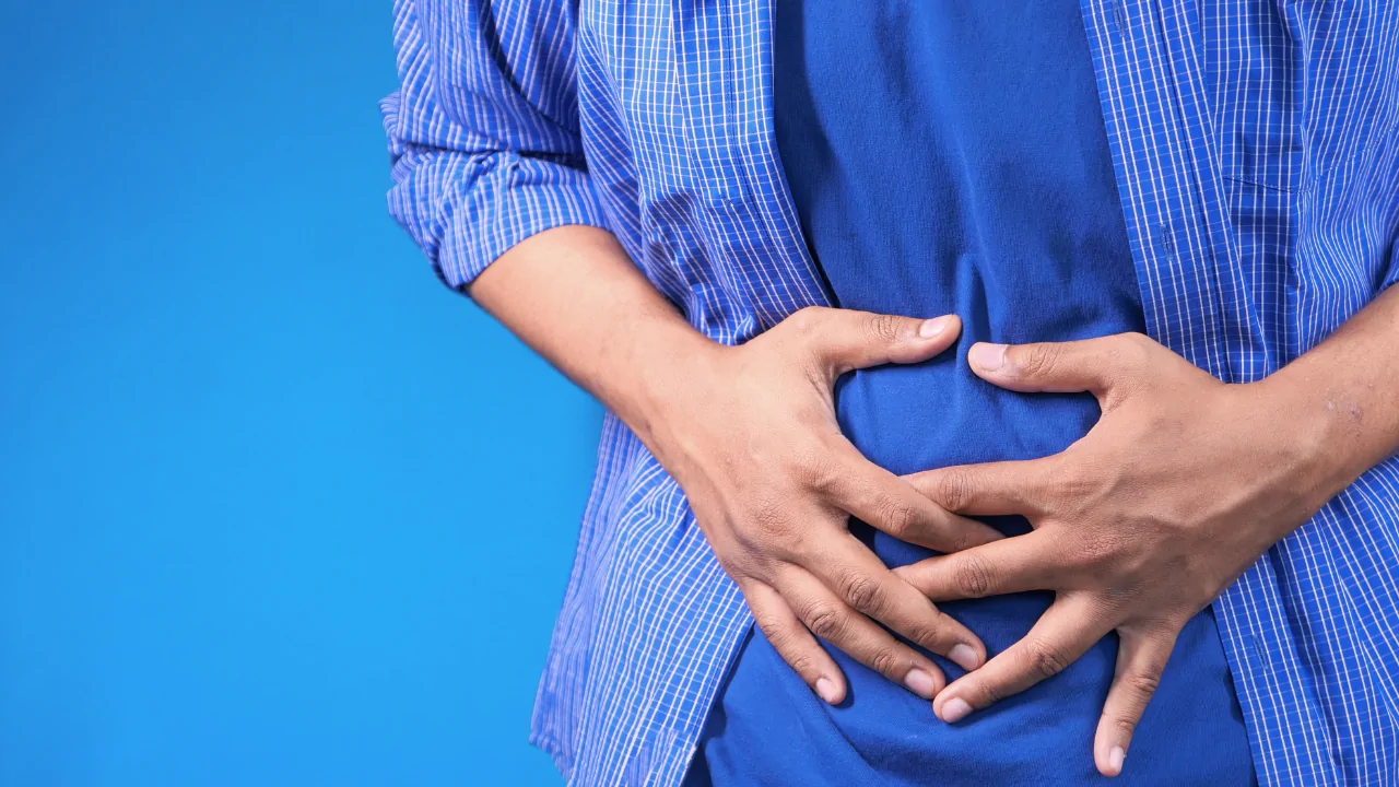 A man in a blue shirt holding his stomach in pain to highlight the need for a digestive issues chiropractor at Spine and Joint Center in Fort Lauderdale.