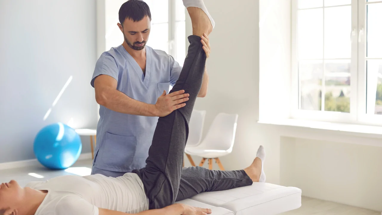 A chiropractor in light blue scrubs performing a passive range of motion stretch on a patient's leg to represent the specialized care provided by a knee pain chiropractor at Spine and Joint Center in Fort Lauderdale.