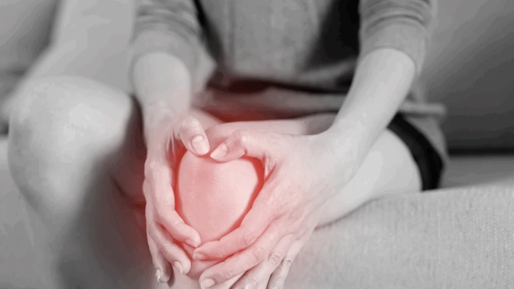 A black and white close-up of a person holding their knee in distress, with a red glowing overlay pinpointing the source of discomfort to represent the services of a knee pain chiropractor at Spine and Joint Center in Fort Lauderdale.