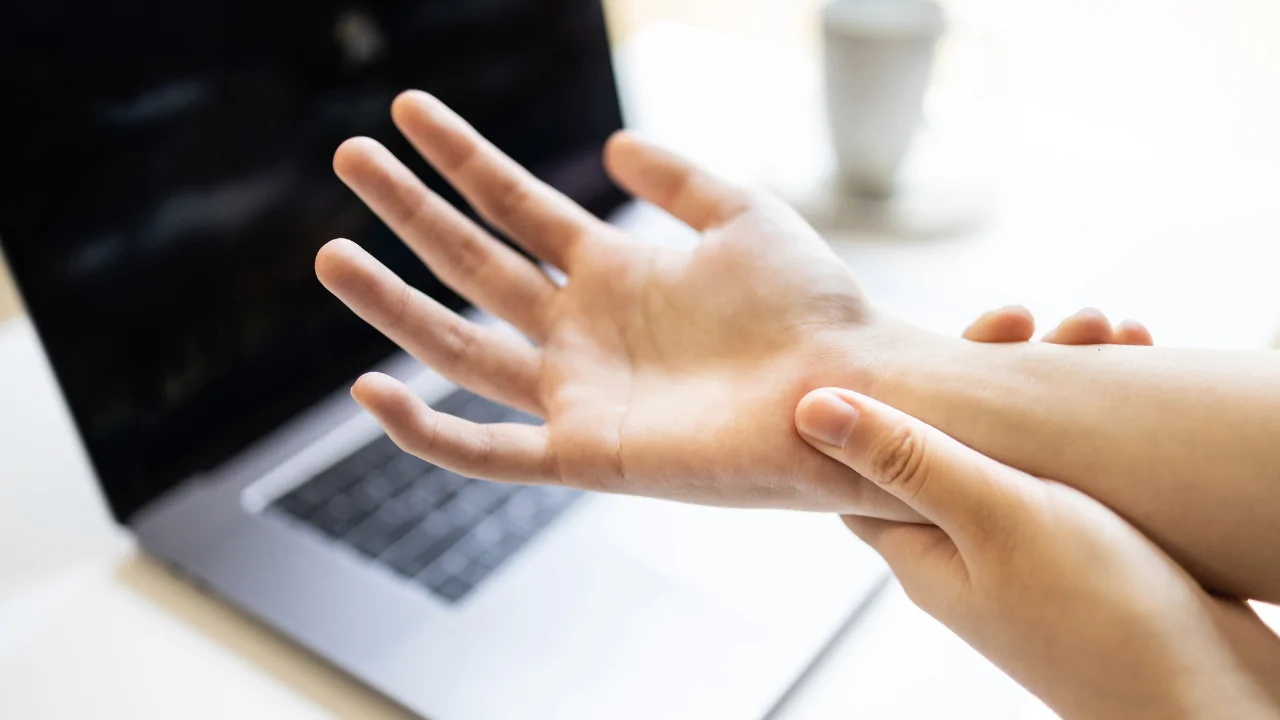 A person sitting at a laptop and holding their wrist in pain to illustrate the need for a neuropathy treatment chiropractor at Spine and Joint Center in Fort Lauderdale.