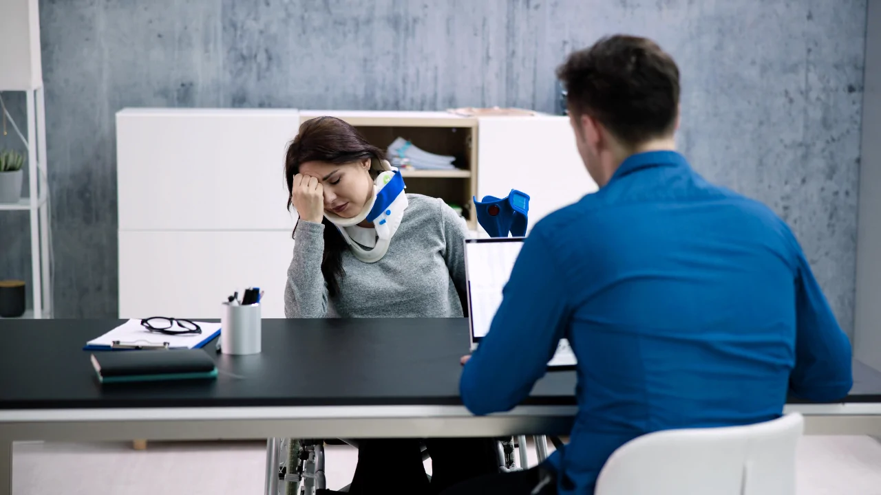 A female office worker wearing a neck brace and sitting in a wheelchair while consulting with a specialist, highlighting the necessity of an office worker chiropractor in Fort Lauderdale for managing desk-job injuries.