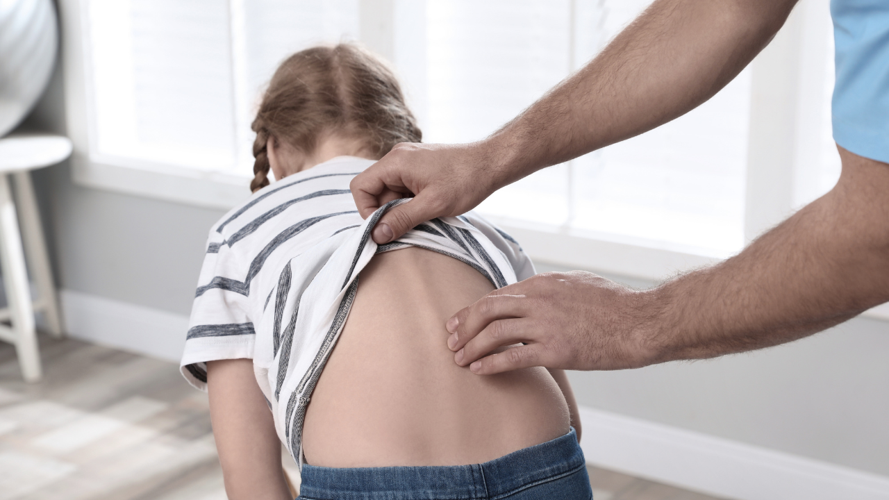 A chiropractor’s hands gently palpating the spine of a young girl to perform a diagnostic assessment for scoliosis pain treatment at Spine and Joint Center in Fort Lauderdale.