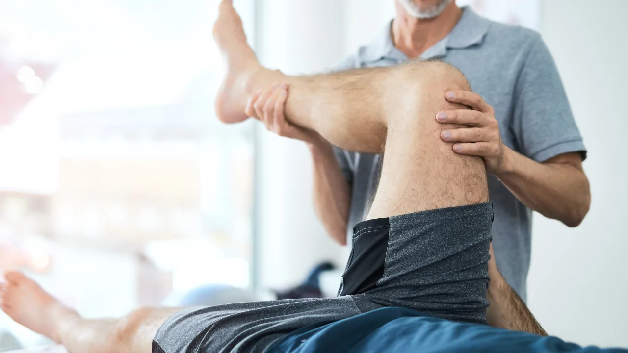 A clinician in a grey shirt performing a manual knee and hamstring stretch on a male patient to provide sprains & strains treatment at a chiropractic clinic in Fort Lauderdale.