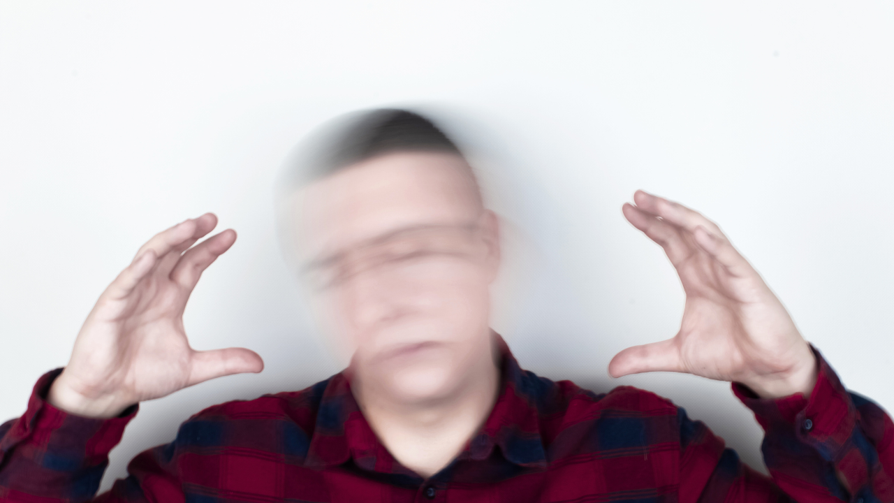 A man in a red flannel shirt with a motion blur effect on his face to illustrate the spinning sensation and need for vertigo and dizziness treatment at Spine and Joint Center in Fort Lauderdale.