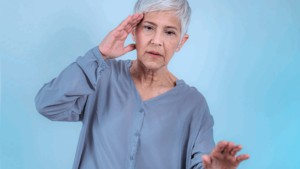An older woman with short gray hair holding her hand to her head and looking confused while reaching out for balance to illustrate the need for vertigo and dizziness treatment at Spine and Joint Center in Fort Lauderdale.