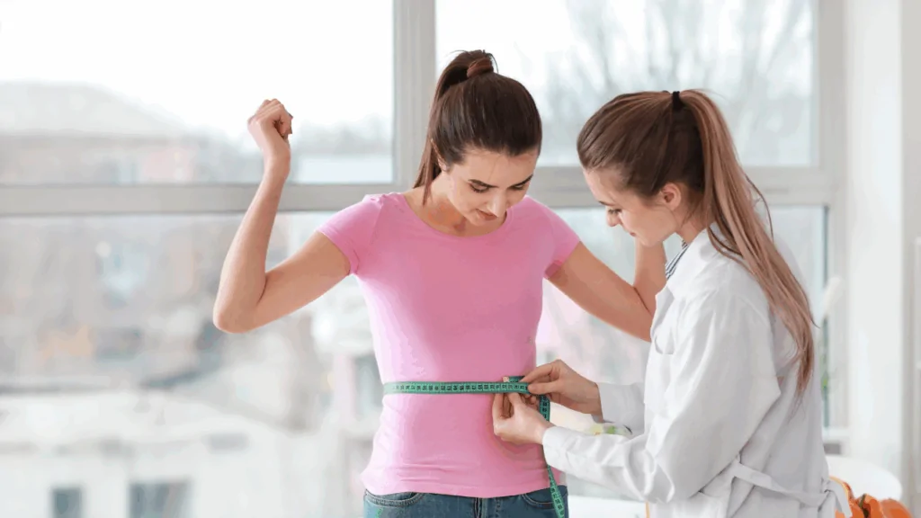 A healthcare professional in a white coat measuring a young woman's waist with a tape measure to track progress in a specialized chiropractic weight loss program in Fort Lauderdale.