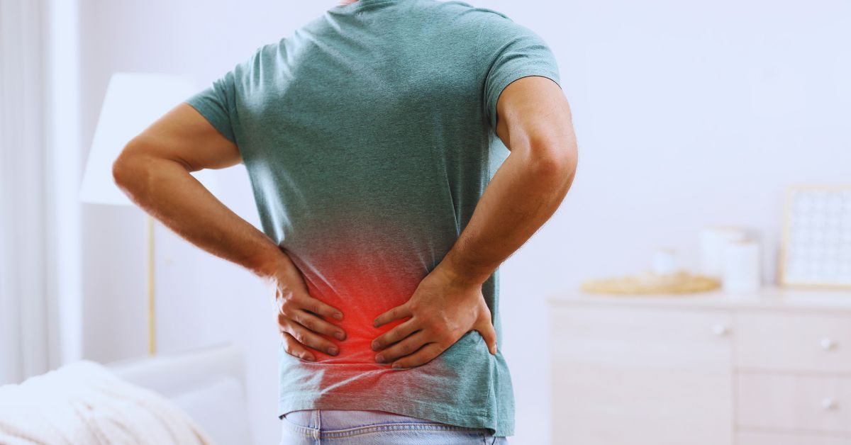 A man standing with his back to the camera and clutching his lower back, which is highlighted with a red glowing area to symbolize chronic pain and inflammation at Spine and Joint Center in Fort Lauderdale.