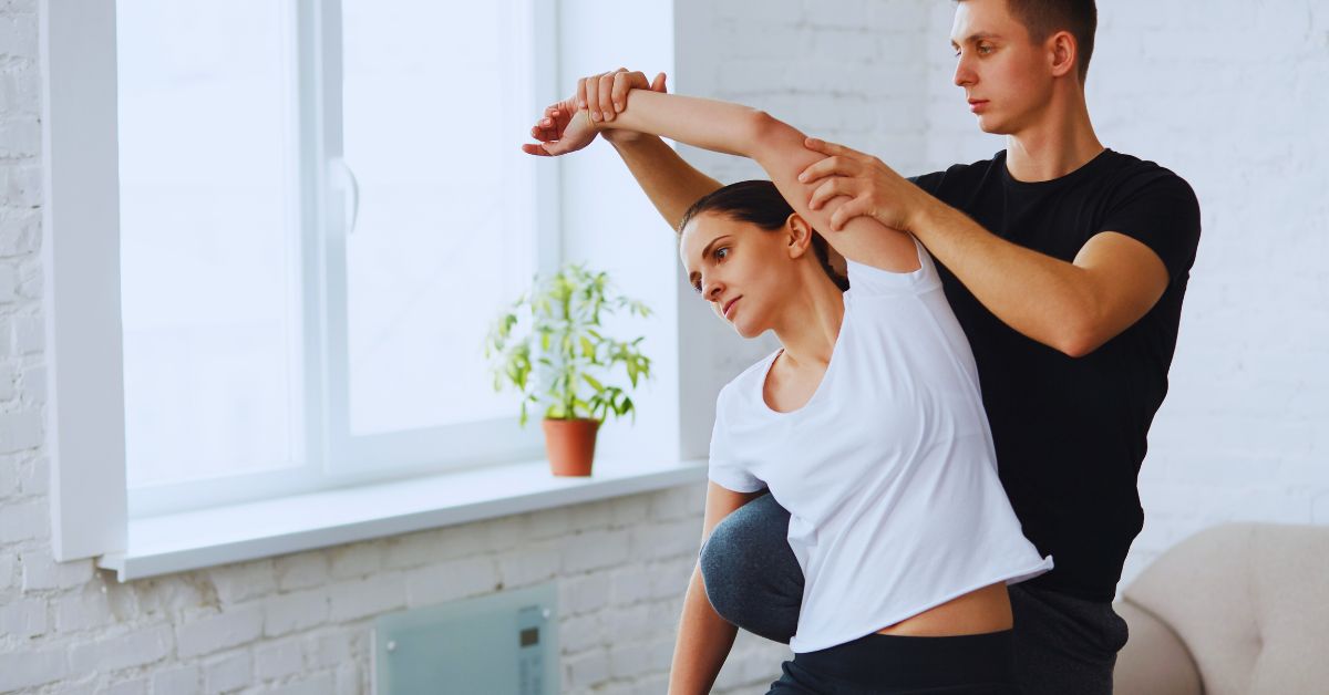 A chiropractor in a black athletic shirt performing a guided triceps and shoulder stretch on a female athlete to provide specialized post-workout recovery care at Spine and Joint Center in Fort Lauderdale.
