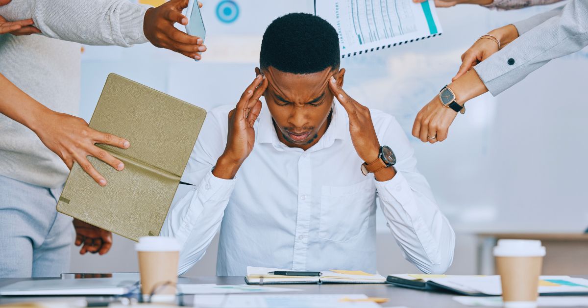 A man in a white shirt sitting at a desk and clutching his temples in distress to illustrate the need for stress and anxiety reduction at a chiropractic clinic in Fort Lauderdale, FL.