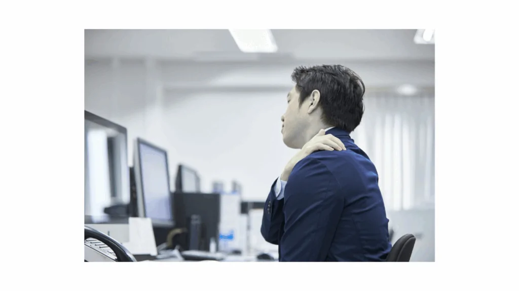 A businessman in a suit sitting at a desk and touching his sore shoulder to illustrate the need for tech neck treatment at Spine and Joint Center in Fort Lauderdale.