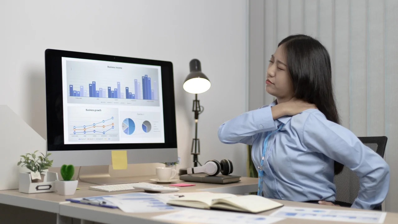 A professional woman experiencing shoulder discomfort at her desk, illustrating the value of a workplace ergonomic assessment in Fort Lauderdale.